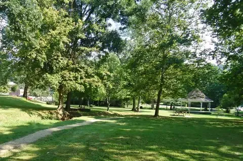 a field with trees and a path that leads to a gazebo in the distance